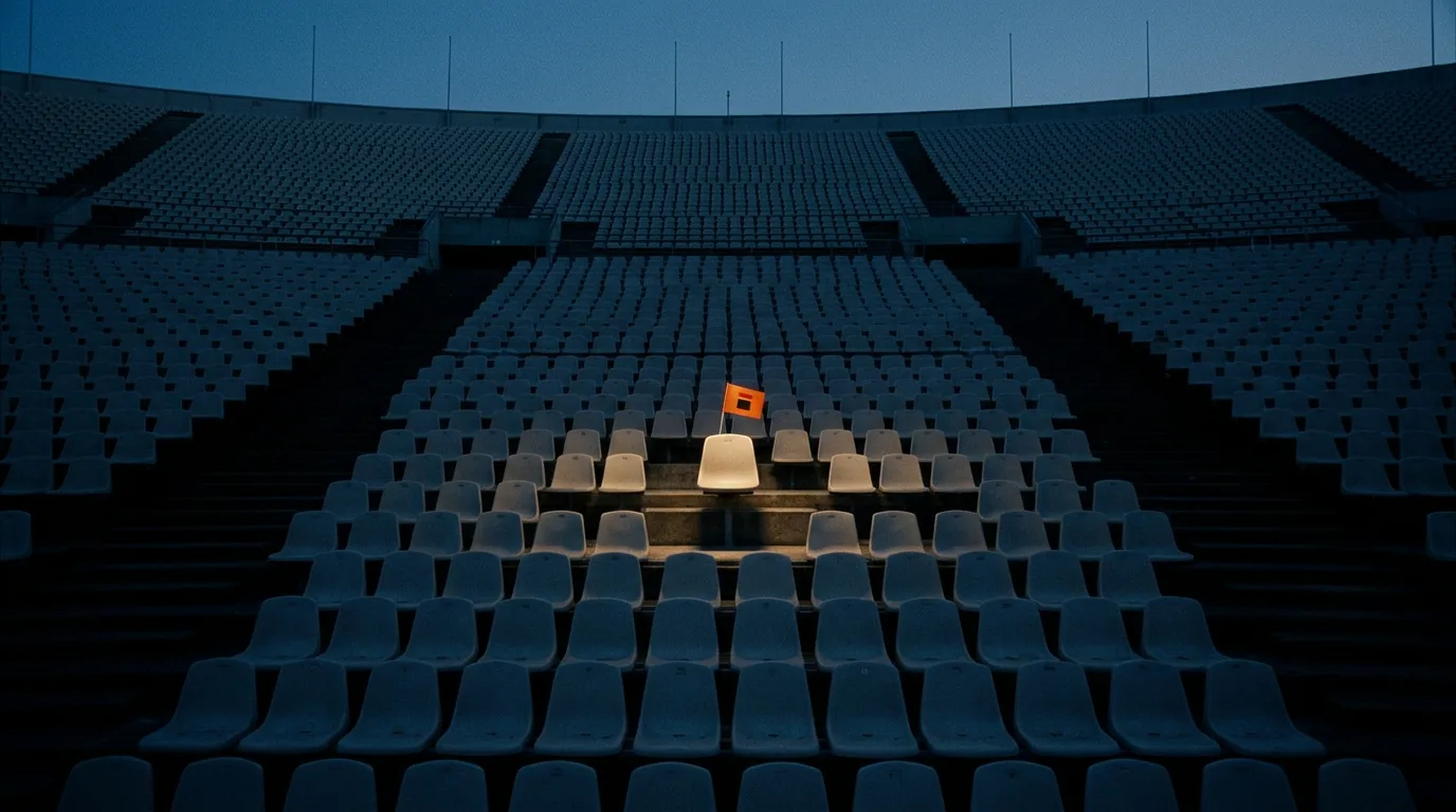 An empty stadium at dusk with every seat in shadow except one, lit by a single spotlight.